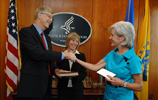 NIH Director Francis Collins and HHS Secretary Kathleen Sebelius shaking hands after he is sworn in with his wife, Diane Baker, looking on
