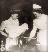 Nurses weighing a baby at the Cincinnati, OH, pure milk station, circa 1908.