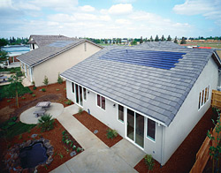 Photo of a gray house with blue solar modules that are integrated in the gray, shingled roof. The home is surrounded by a wooden fence and backyard.