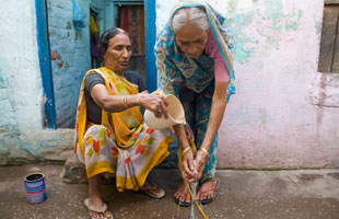 Two older women help each other to wash their hands