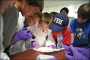 Students from Anne E. Moncure Elementary School in Stafford, Virginia examine evidence while participating in a mock case investigation at Hogan’s Alley (on the grounds of the FBI Training Academy in Quantico, Virginia). During the exercise, students learned about the many different and important components of investigating cases and bringing criminals to justice. The students are part of a mentoring program supported by FBI employees in the Training, Laboratory, and Operational Technology Divisions at Quantico. 