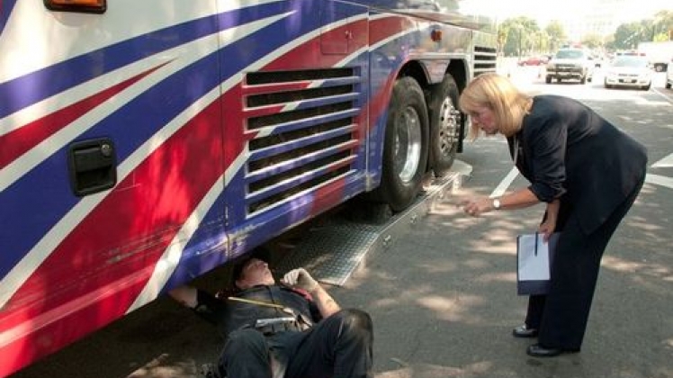 A safety inspector conversing with a mechanic who is checking the underside of a bus.