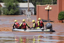 Image of rescuers in boat on flooded city street. Click for larger image.