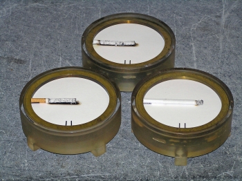 Examples of results of the Standard Test Method for Measuring the Ignition Strength of Cigarettes (ASTM E2187) are shown. Non-filter (top) and filter (left) cigarettes "failed," having burned the full length in the test. The cigarette that extinguished before burning its full length (right) passed. The test calls for performing 40 such determinations for each cigarette and reporting the number of full-length burns. Cigarettes are positioned on the standard ASTM E2187 test substrate.