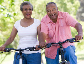 Photograph of an older couple riding bikes outside.