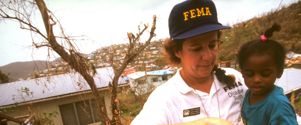 A FEMA worker carrying a child away from disaster area