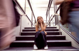 Sad girl sitting on steps at school as students pass by her