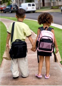 Young children walking to school with backpacks and lunches.