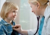 A little girl at office visit  with female doctor checking her chest with stethoscope.
