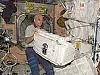 An astronaut moving large, white cargo containers around in the International Space Station