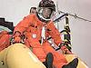 An astronaut in an orange launch and entry suit practices going down a crew escape slide