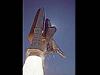 Against a dark blue sky, exhaust shoots out of the nozzle of a solid rocket booster during a shuttle launch