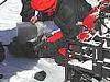 A small black meteorite lies in the snow while a man dressed in black and red winter clothing documents where it was found