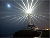 Picture of lighthouse giving off light against a dark sky with the moon in the background