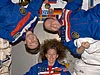 Three astronauts float, with two sideways and one right side up