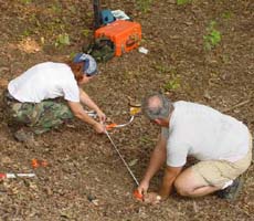 (photo) Two archeologists use measuring tapes. (Midwest Archeological Center)