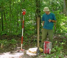 (photo) An archeologist plants an orange-and-white datum point on a stick in concrete. (Midwest Archeological Center)