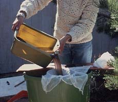 (photo) An archeologist dumps water through fine mesh into a bucket. (NPS)