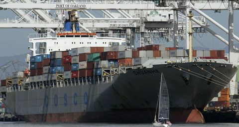 Date: 04/27/2011 Description: A boat sails past a cargo ship waiting to be unloaded at the Port of Oakland, April 27, 2011, seen from Alameda, California. © AP Image