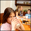A girl drinking a glass of milk, with her family in the background