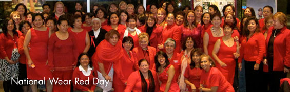 A group of mostly women dressed in red dresses, red shirt, red sweaters sit and stand as they pose for the camera in celebration of National Wear Red Day.