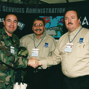 three men, one in uniform, shaking hands