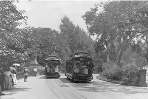 Photo: two trolley cars on the  road, with people walking on the side of the road.