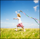 Foto: Una niña corriendo por el campo haciendo volar una cinta