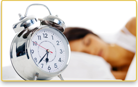 Imagen de un reloj que marca las 6:37. Atrás, una mujer duerme.
