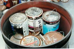 Photo of waste paint cans and other materials placed in a drum for disposal.