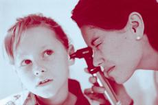 Photograph of a female doctor examining the ear of a young girl