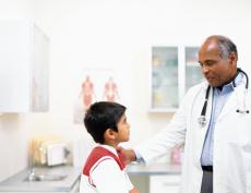Photograph of a male doctor talking to a boy in an exam room