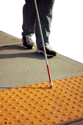 persona invidente caminando con un bastón hacia una señal para peatones en la calle