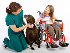 Trabajadora de la salud al lado de una niña en silla de ruedas y un perro