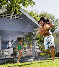 Father playing with children in front lawn sprinkler