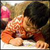 A 3-year-old boy colors in a book on a couch while a Promoting Positive Parenting Program coach helps his  mother fill out a survey.