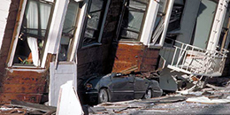 A car crushed beneath a building post-earthquake.