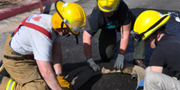 Three structural firefighters in partial gear roll up a hose.