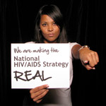 Woman holding sign 'Facing AIDS by making the National HIV/AIDS Strategy REAL.'