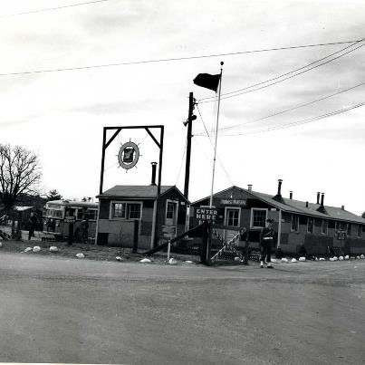 Photo: Camp Myles Standish was a U.S. Army camp located in Taunton, Massachusetts. It functioned as a prisoner-of-war camp, a departure area for about a million U.S. and Allied soldiers; and a candidate site for the United Nations Headquarters, soon after the military camp closed. The camp functioned as the port of embarkation, a quartermaster was set up so an entire division could be prepared for deployment within a day. German soldiers who were captured during the war were detained at this camp. Also, Italian soldiers were detained there as well although they were considered 'co-belligerents' because Italy had surrendered by the time the Italian soldiers arrived at Camp Myles Standish. The camp closed in January 1946 following World War II. The site of Camp Myles Standish was briefly considered as a possible site for the United Nations. This is a Photograph of the front gate of the camp with the provost marshal’s office the first building seen by all who entered the gates. Notice on the left side of the photograph a bus of new soldiers just arriving at the main gate. RG 336, Records of the Boston Port of Embarkation.