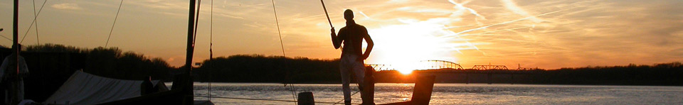 photo of a replica keelboat with a crew member on the bow at sunset