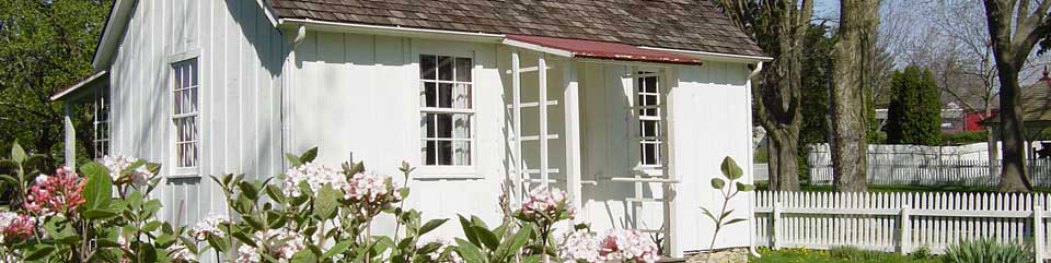 Pink flowers blossom in the garden of a white two-room cottage.