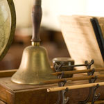 Pencils, books, a hand bell, and a globe sit atop a schoolhouse desk.