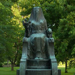 A bronze statue of an Egyptian goddess sits among park greenery.