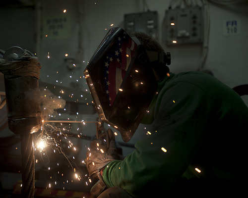 Image description: U.S. Navy Aviation Boatswain&#8217;s Mate Equipment 3rd Class Devin McMaster welds an anchor terminal on an arresting gear cable aboard the aircraft carrier USS George Washington in the Pacific Ocean.
Photo by U.S. Navy Mass Communication Specialist 3rd Class William Pittman