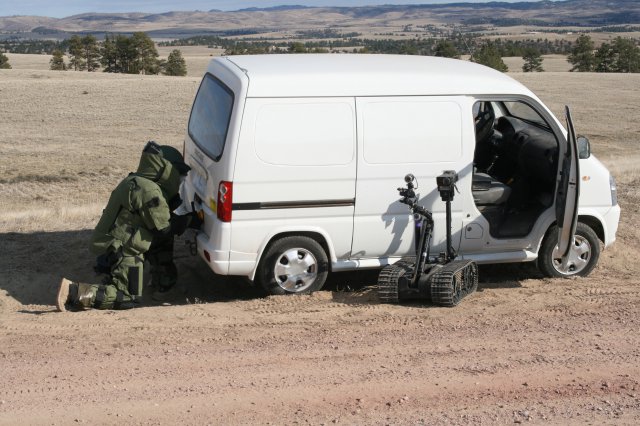 Staff Sgt. Andrew Olson, 663rd Ordnance Company, 242nd Explosive Ordnance Disposal Battalion, 71st Ordnance Group (EOD), kneels as he sets up a device to open the trunk of a van remotely after the robot was unable to engage the handle of the door. The Oct. 9, 2012, training scenario mimics threats EOD technicians face both stateside and in combat.
