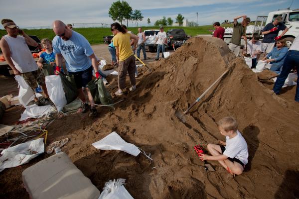 Nicholas Boesl plays in the sand as his mother and sister fill sandbags at the Sertoma Sports Complex. Residents are sandbagging along the Souris River to try to prevent flooding.