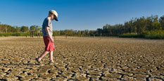 Boy walking across a field that has no grass because of a drought