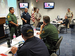 Robert C. Gomez CBP Incident Commander, center, discusses CBP response efforts with an integrated staff working the Incident Command Post located at the CBP New Orleans Air and Marine Branch.