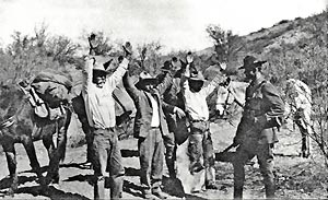 1926, near Tucson, Arizona. Two U.S. Immigration Service Border Patrol Inspectors guard and search liquor smugglers, plus relieve them of the guns.